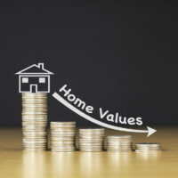 STACKED US QUARTER COINS ON WOODEN TABLE WITH WHITE ILLUSTRATION SHOWS DECREASING OF HOME VALUES / FINANCIAL CONCEPT