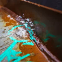 Close-up of rusty metal surface with blue paint markings and water droplets
